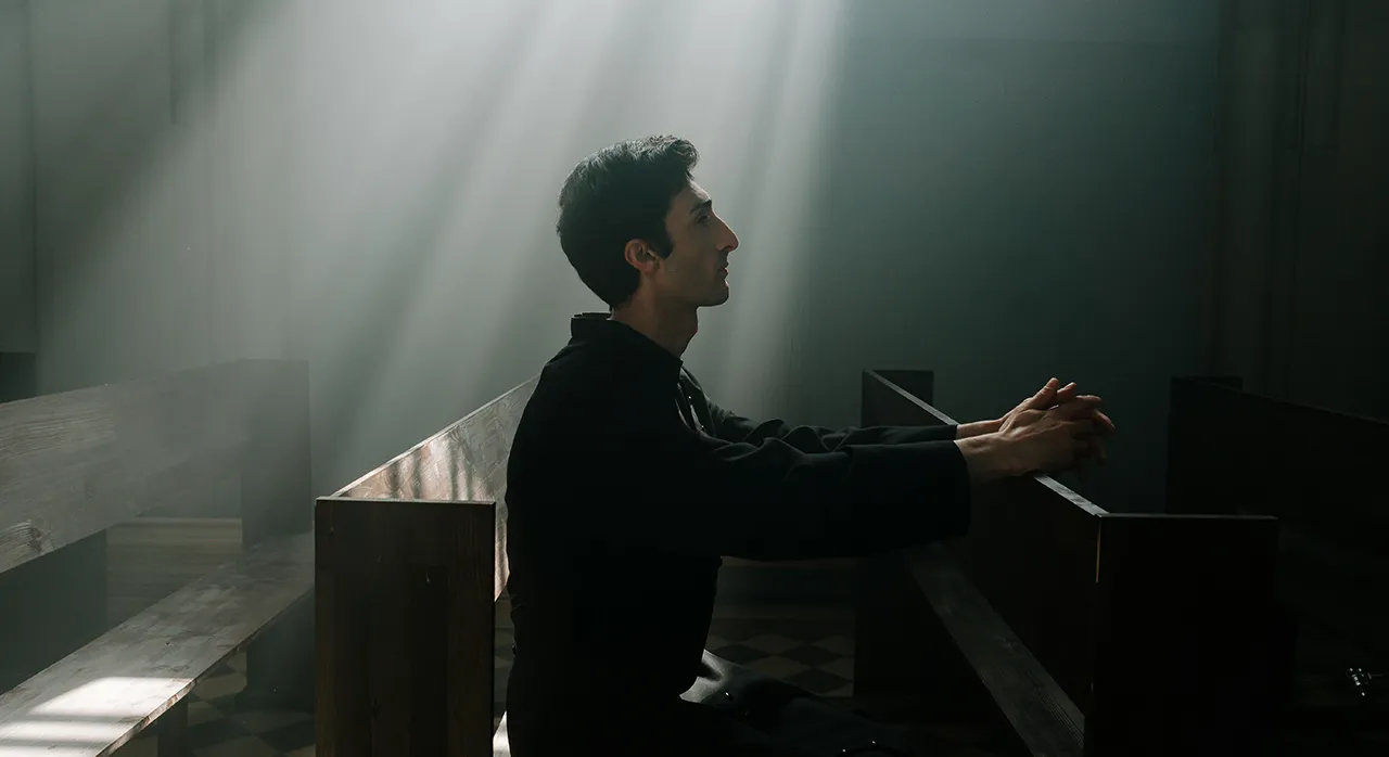 Un hombre arrodillado en una iglesia, iluminado por un haz de luz, simbolizando la búsqueda de la verdad bíblica sobre la homosexualidad.